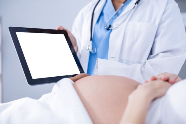 Doctor showing ultrasound scan on to pregnant woman on digital tablet in hospital