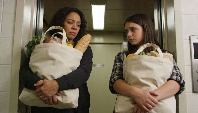 Mother and teen daughter carrying grocery totes looking concerned in elevator