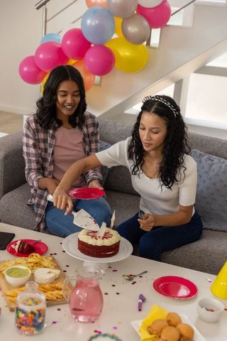 African american mother and teenage daughter cutting red velvet cake at home party