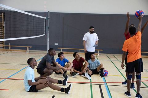 Teen boys practicing volleyball in school gym during coach-led training
