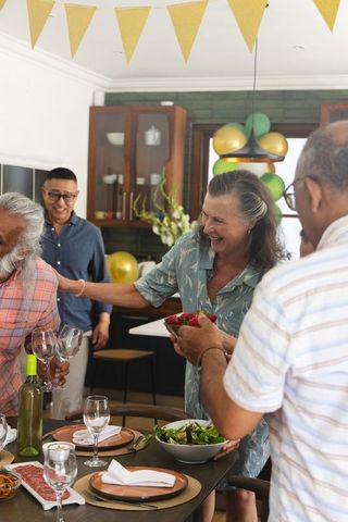 Multigenerational friends gathering around kitchen table sharing food, wine, laughter