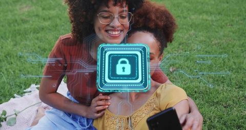 Smiling friends sharing smartphone on lawn with glowing digital padlock symbolizing privacy