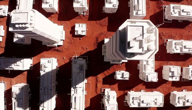Aerial view of futuristic white buildings on red soil with octagonal tower and shadows