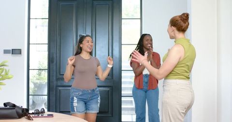 Diverse women greeting friends in bright modern entryway celebrating reunion
