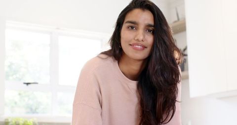 Elegant indian woman in minimalist kitchen leaning on countertop