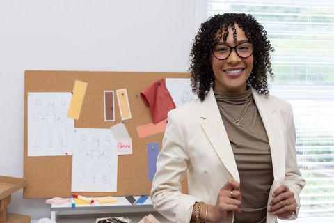 African american fashion designer smiling in studio holding blazer lapels with corkboard
