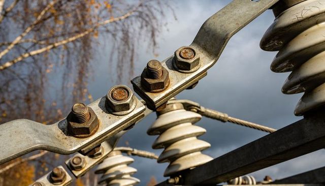 Rusting bolted clamp gripping ceramic insulators on utility pole under storm clouds
