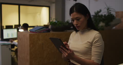Asian Businesswoman Using Tablet Late in Modern Office Environment
