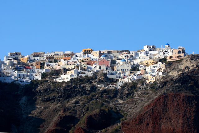 This image showcases the traditional whitewashed houses of Oia, a picturesque village perched on the cliffs of Santorini, Greece. A blue sky enhances the vibrant aura of the Mediterranean setting. Ideal for use in travel blogs, tourism promotions, brochures, posters, and websites emphasizing European travel and vacation destinations.