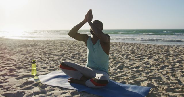 Focused african american man practicing yoga on beach, exercising outdoors by the sea. fitness, healthy and active lifestyle concept.