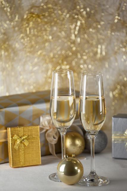 Two champagne flutes and Christmas gifts against golden color decoration