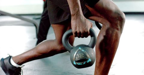 African american man lunging while holding kettlebell marked 12 for strength training