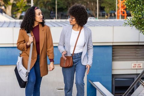Two women walking and talking on urban stairs carrying tote and crossbody bag