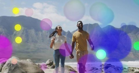 Romantic Black Couple Walking and Holding Hands on Rocky Beach with Mountain Backdrop