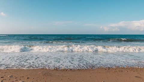 Sunlit breaking waves rolling onto sandy shore with white foam and pebbles