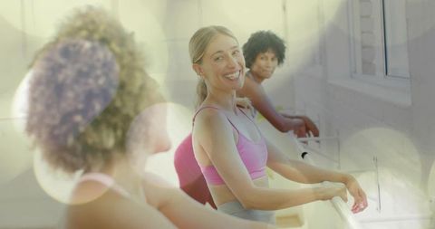 Smiling woman practicing barre workout in sunlit studio with group fitness energy
