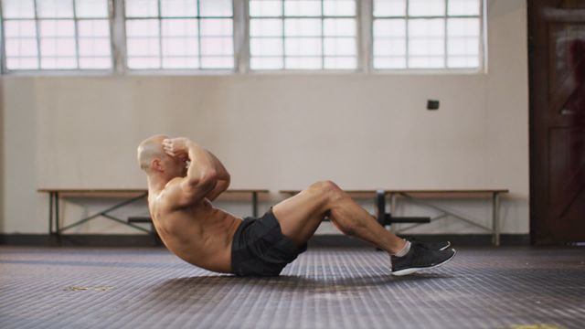 Man performing sit ups in an indoor gym, wearing shorts and sneakers. Ideal for content related to fitness, workout routines, health, and exercise programs.