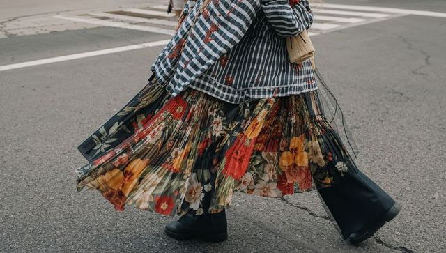 Walking across urban crosswalk wearing pleated floral skirt, striped denim jacket, boots