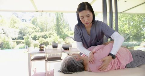 Physiotherapist supporting senior woman during outdoor rehabilitation on sunlit terrace