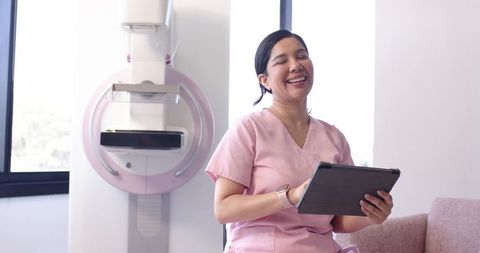 African American Nurse Smiling While Holding Tablet Next to Mammography Unit