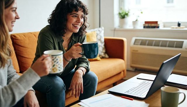 Friends enjoying coffee while watching laptop in cozy apartment living room remote work