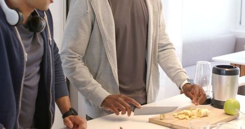 Young male friends preparing banana smoothie on kitchen island in bright modern space