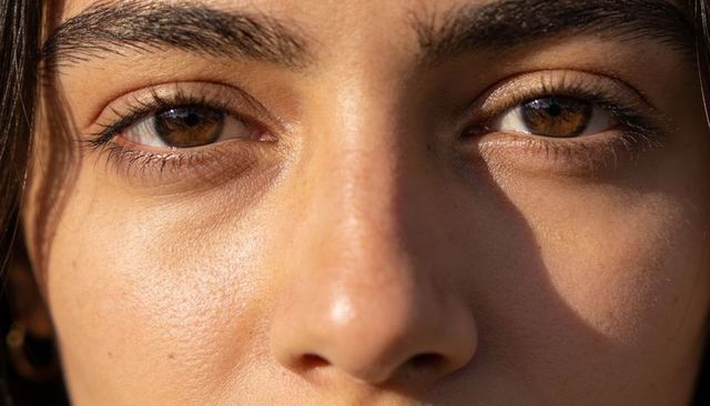 Hazel-eyed woman-presenting closeup showing natural skin texture and warm sunlit gaze