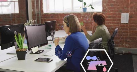 Professional woman wearing headset typing at open-plan office desk with tech overlay