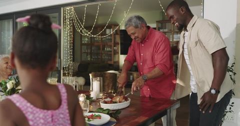 Multigenerational family carving roast at candlelit dining table sharing holiday meal
