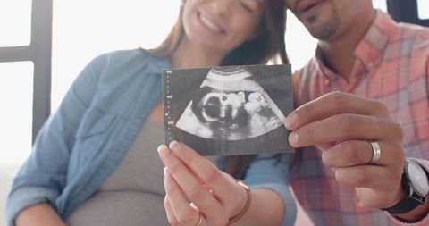 Expecting parents holding ultrasound by window with smiles