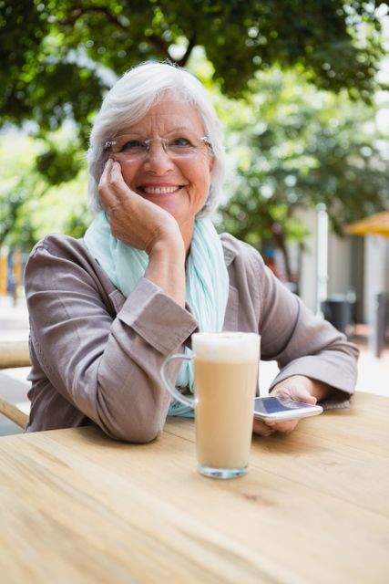 Portrait of senior woman holding mobile phone in outdoor cafÃ©