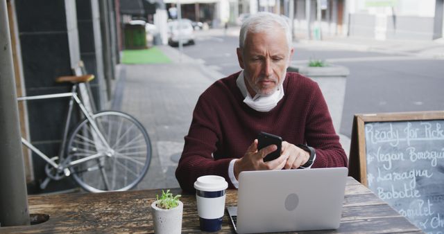 Older man working on laptop and smartphone at outdoor cafe - Download Free Stock Images Pikwizard.com