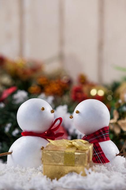 Two snowmen with a Christmas gift in a festive setting. Ideal for holiday greeting cards, festive decorations, winter-themed advertisements, and seasonal promotions. Perfect for conveying holiday cheer and the spirit of giving.