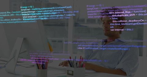 Male developer typing at desk with translucent code overlay in modern office workstation