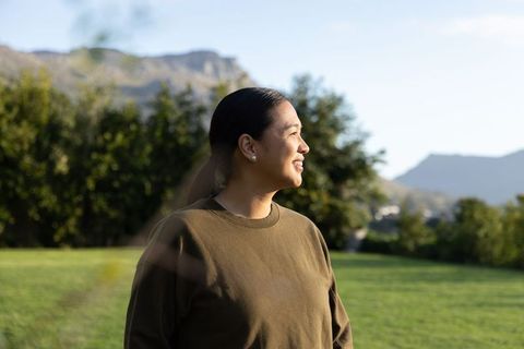 Asian woman smiling in olive crewneck enjoying golden hour meadow and mountain view