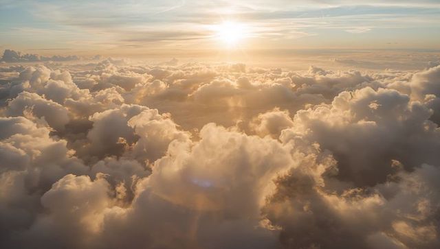 Glowing golden cloudscape casting sunbeams over cumulus sea from aircraft at sunset