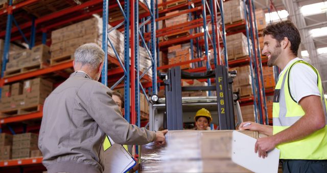 Workers in warehouse wearing safety vests, collaborating and organizing inventory using forklift. Useful for themes related to logistics, teamwork, supply chain management, and industrial efficiency. An ideal visual for articles and materials discussing warehouse management, workplace safety or operational processes in distribution centers.