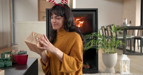 Woman Enjoying Gift by Fireplace in Cozy Holiday Setting