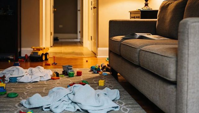 Living room showing post-play clutter with blankets, blocks, trucks, open book