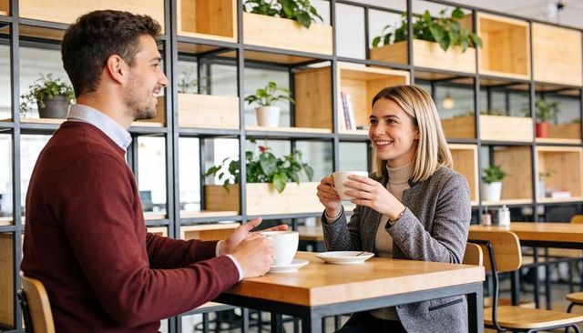 Colleagues chatting over coffee in modern coworking cafe with plants and wooden shelving