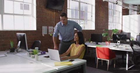 Female professional collaborating with male colleague at modern open-plan office workspace