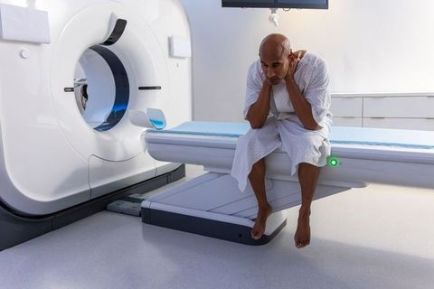 Anxious african american male sitting on mri table holding neck before scan