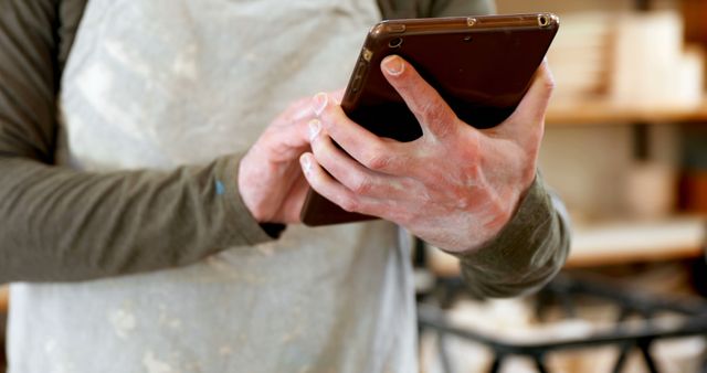 Carpenter using a tablet for planning and design in a woodworking workshop. Hands covered in sawdust highlight manual labor combined with technology. Perfect for illustrating modern carpentry, digital tools in craftsmanship, or showcasing integration of technology in traditional trades.