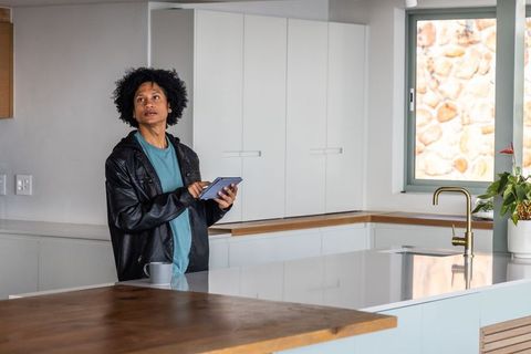 Young african american man holding tablet in minimalist kitchen glancing up with coffee