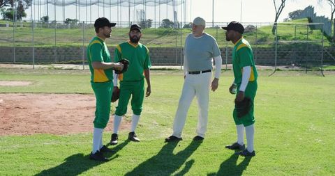 Senior coach guiding diverse baseball teammates listening on sunny infield during practice