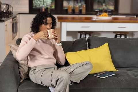 Non-binary person sipping coffee on gray sofa, cozy minimalist modern open-plan living