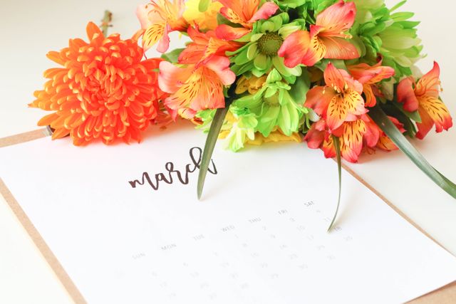 Captures a colorful flower arrangement next to a March calendar sheet. Ideal for content related to seasonal planning, spring events, or decor. Useful for blogs, social media posts about time management, calendars, floral arrangements, or spring themes.