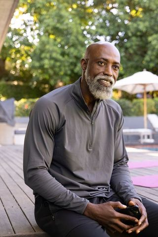 Senior african american man relaxing poolside after yoga holding smartphone