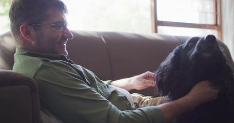 Smiling man relaxing on sofa while petting beloved dog