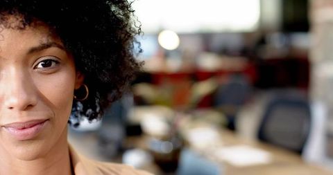 Confident professional woman headshot in modern office with warm bokeh background